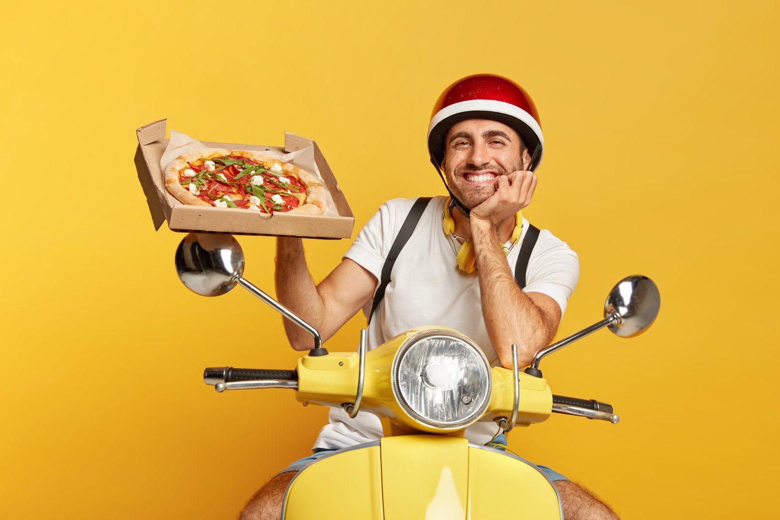 friendly-looking-deliveryman-with-helmet-driving-yellow-scooter-while-holding-pizza-box-11zon