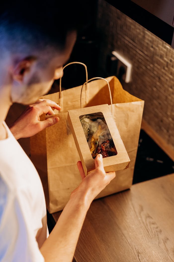A man at home is unpacking a food delivery from a paper bag on a kitchen counter.