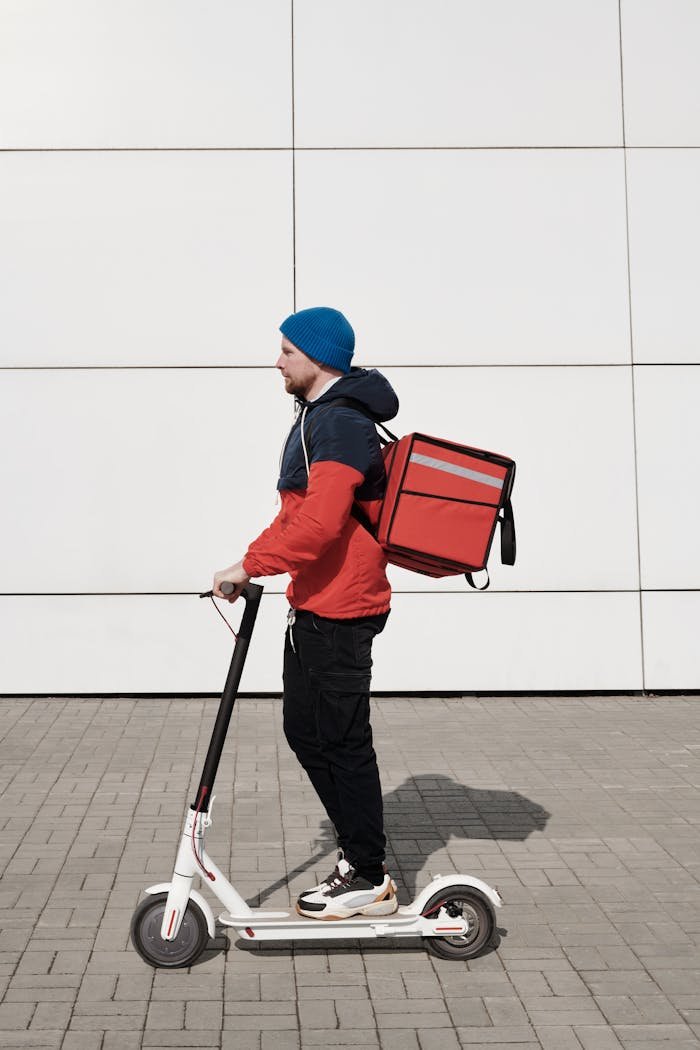 A food delivery person on an electric scooter against a modern building backdrop.