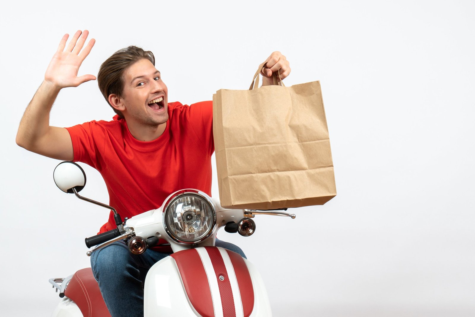 young-smiling-courier-guy-red-uniform-sitting-scooter-holding-paper-bag-saying-hello-white-wall-11zon